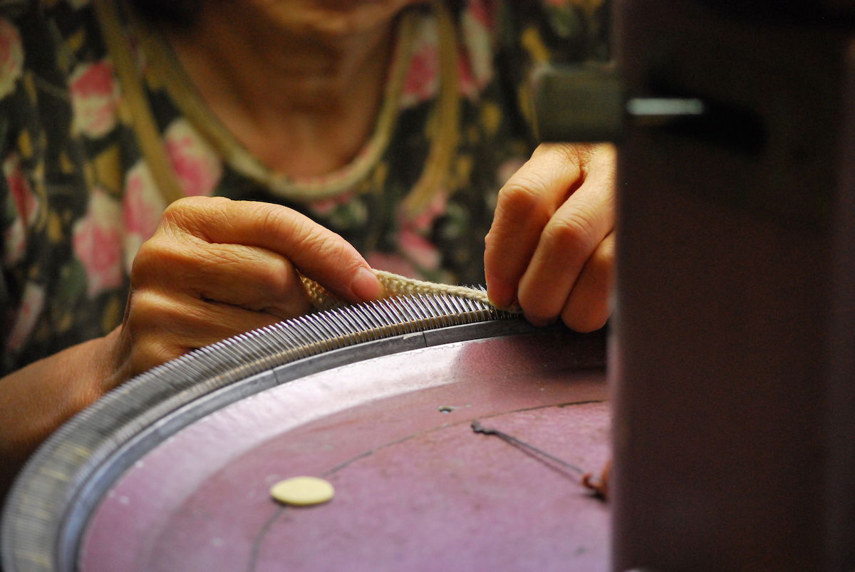 A vintage circular knitting machine being set up by its operator